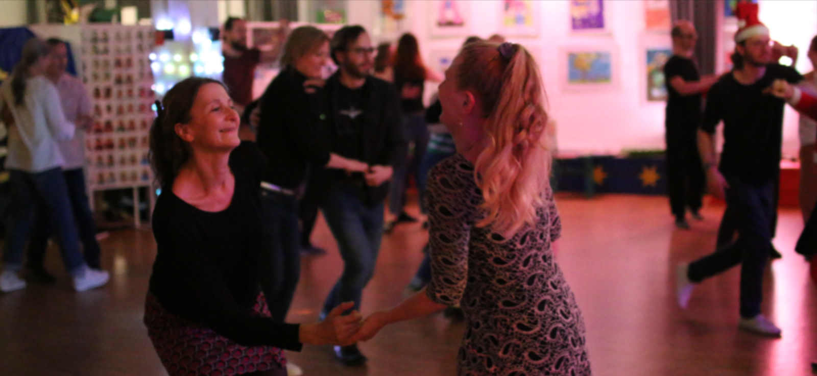 Zwei Frauen tanzen im Vordergrund zusammen, im Hintergrund sieht man weitere Pärchen beim Tanzen.